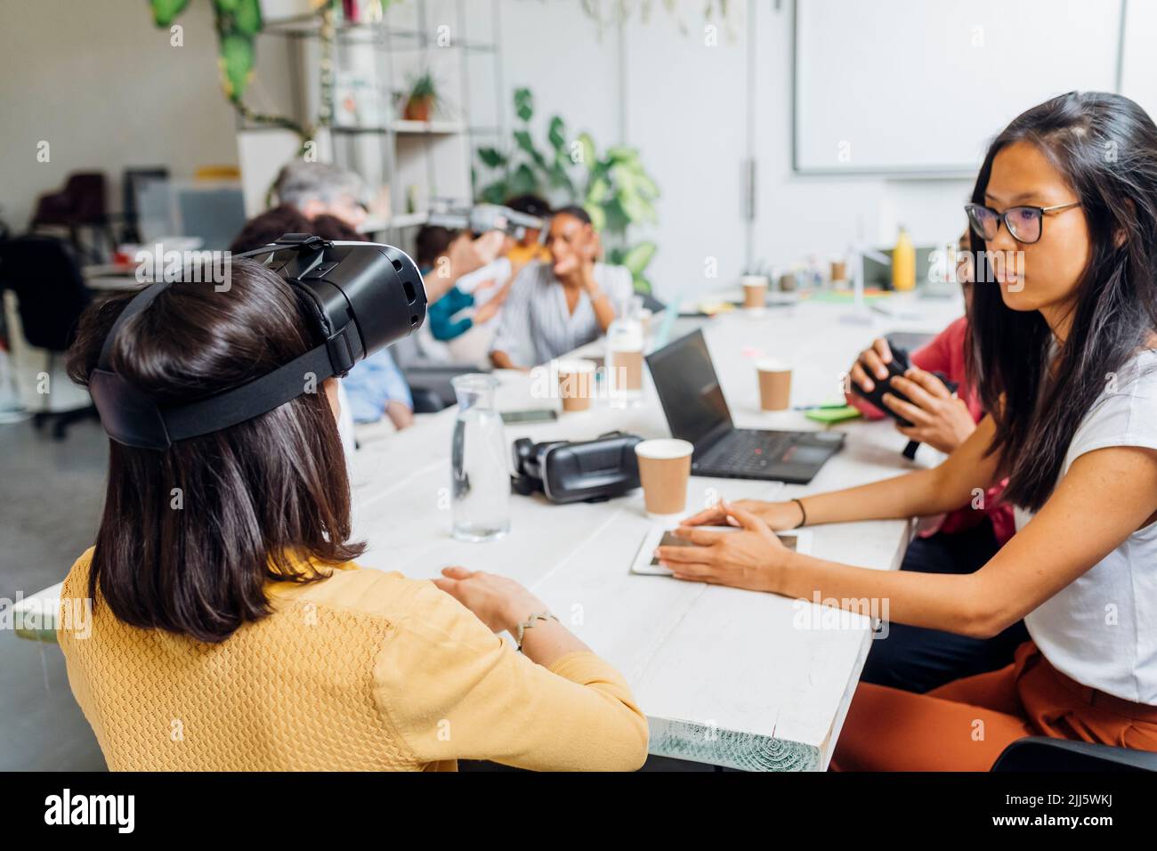 Femme d'affaires avec simulateur de réalité virtuelle par des collègues au bureau Banque D'Images