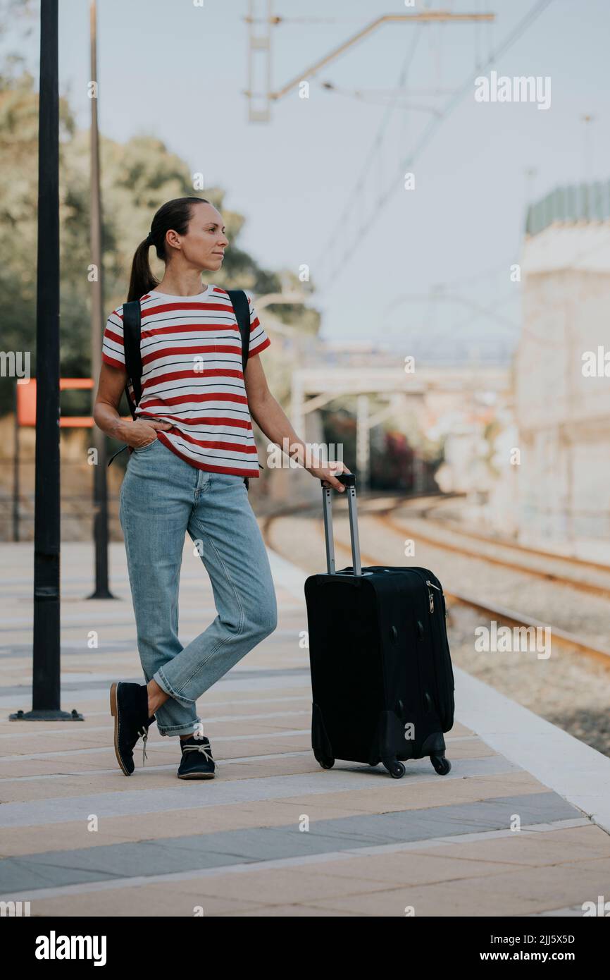 Femme avec une valise attendant le train sur la plate-forme de chemin de fer Banque D'Images