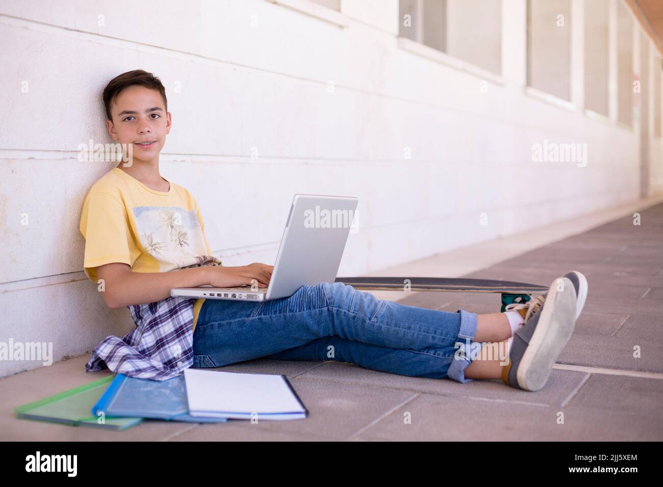 Jeune garçon caucasien souriant assis sur le sol à l'aide d'un ordinateur portable. Espace pour le texte. Banque D'Images