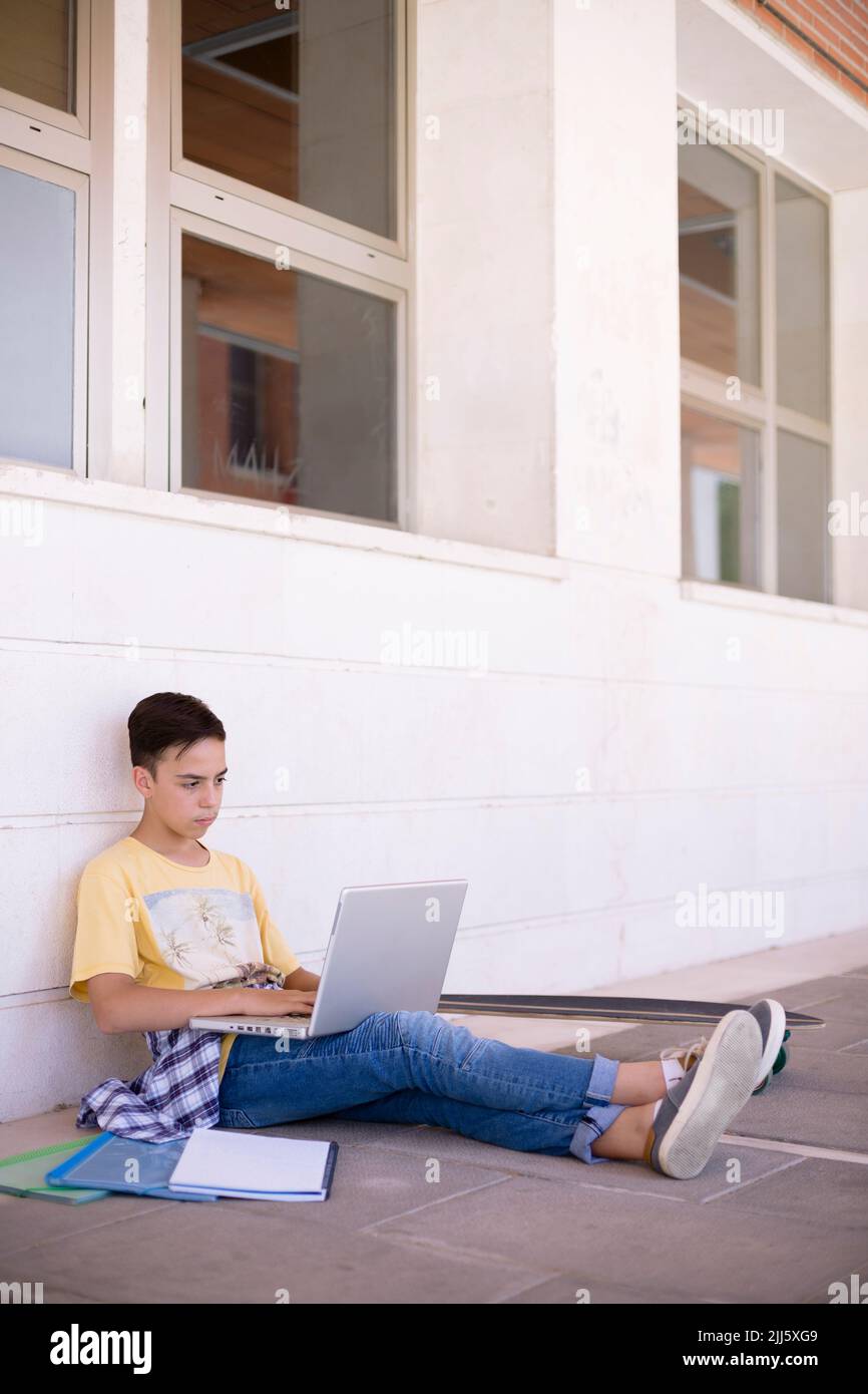 Adolescent caucasien assis sur le sol étudiant avec un ordinateur portable. Espace pour le texte. Banque D'Images