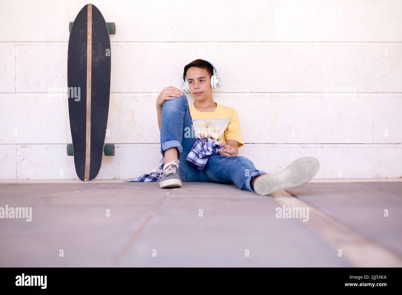 Un garçon caucasien écoute de la musique. Un skateboarder adolescent assis sur le sol. Banque D'Images
