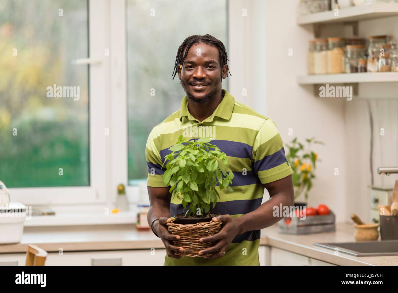 Homme souriant tenant une plante de basilic debout dans la cuisine Banque D'Images