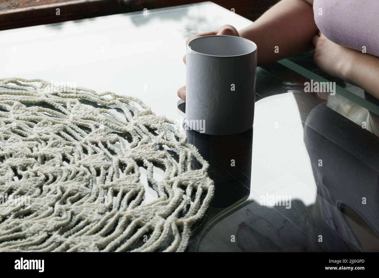 la main de la femme latina tient une tasse blanche sur une table en verre, avec une pièce maîtresse ronde blanche en forme de crocheted. une fille détendue dans son bureau buvant une tasse de café Banque D'Images