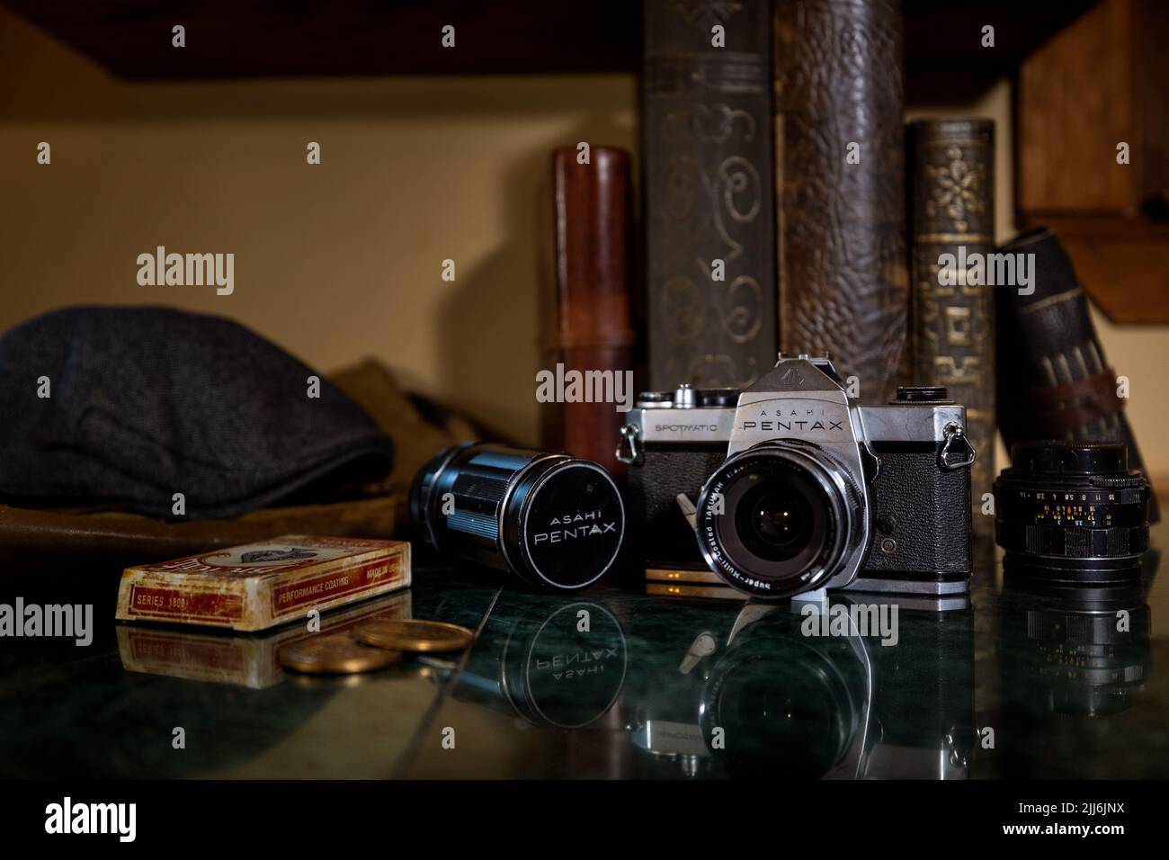 Un gros plan d'un appareil photo Pentax vintage avec objectif Asahi, livres, cartes à jouer et pièces de monnaie sur le comptoir Banque D'Images