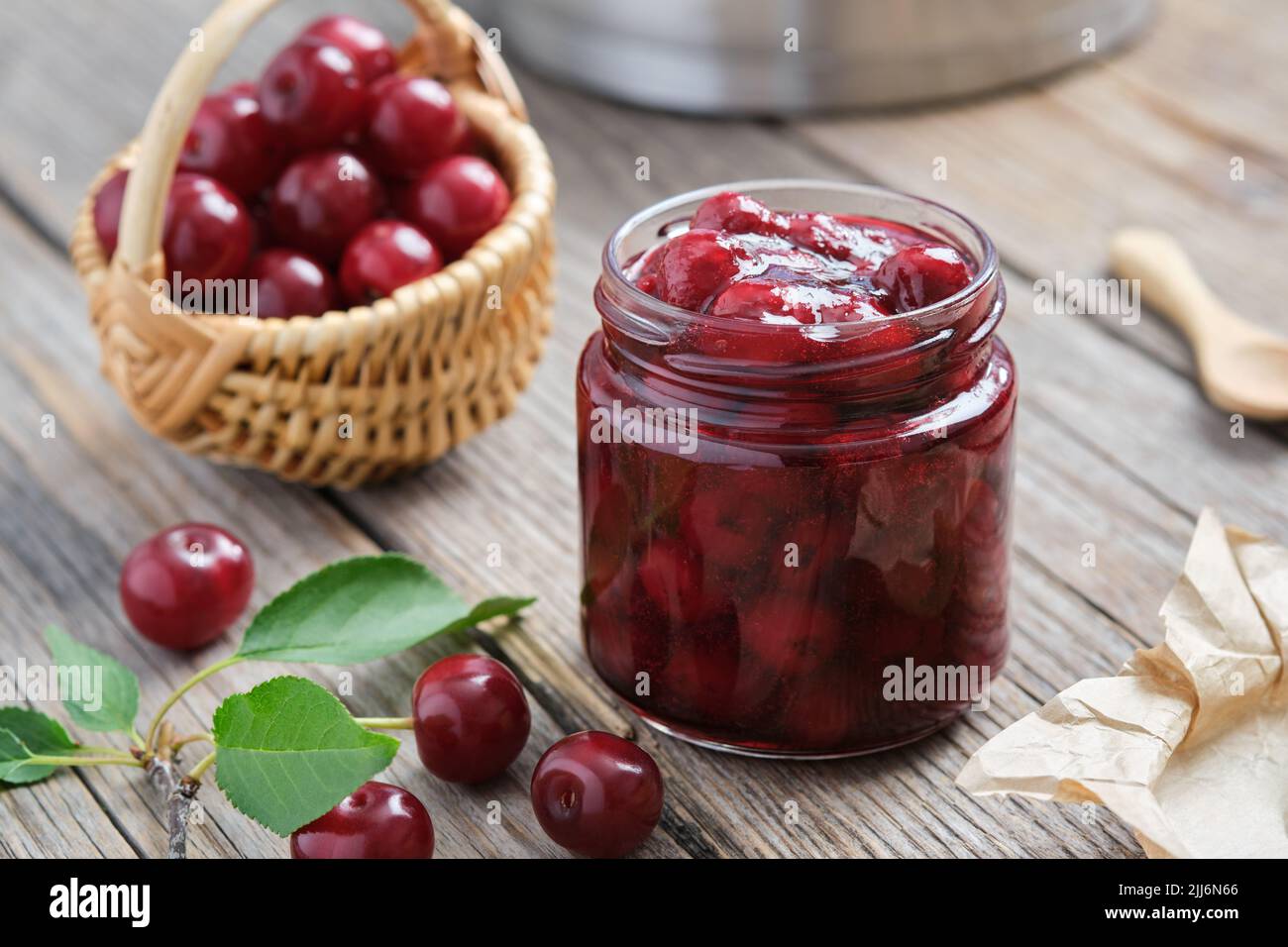 Pot de confiture de cerises maison et panier de cerises mûres sur une table de cuisine. Banque D'Images