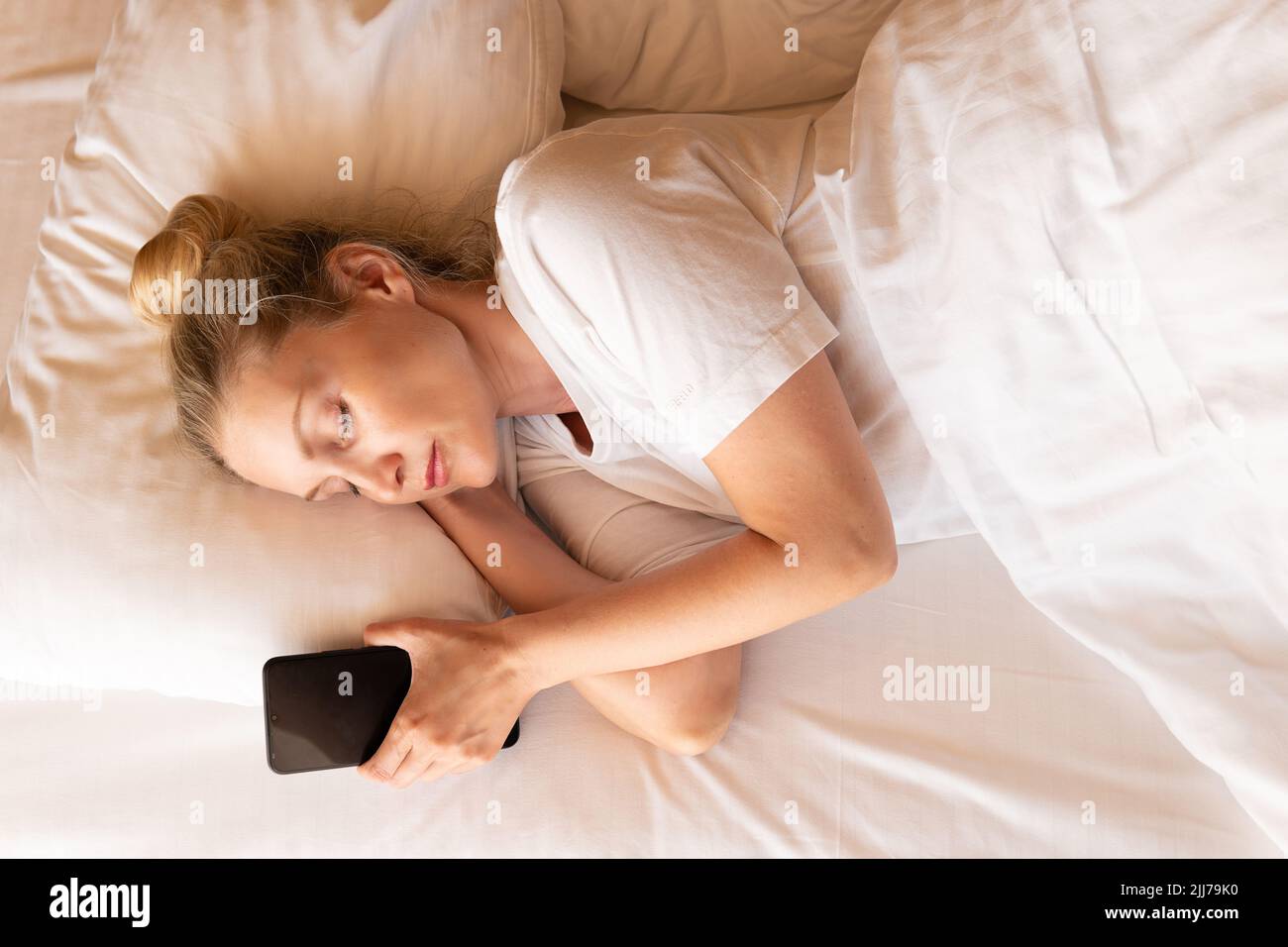 Femme beau téléphone mobile blond sommeil lit couverture de lit couché, de l'oreiller blanc de la cellule pour la sieste calme, positif sain. Un plaisir confortable à l'intérieur, Banque D'Images