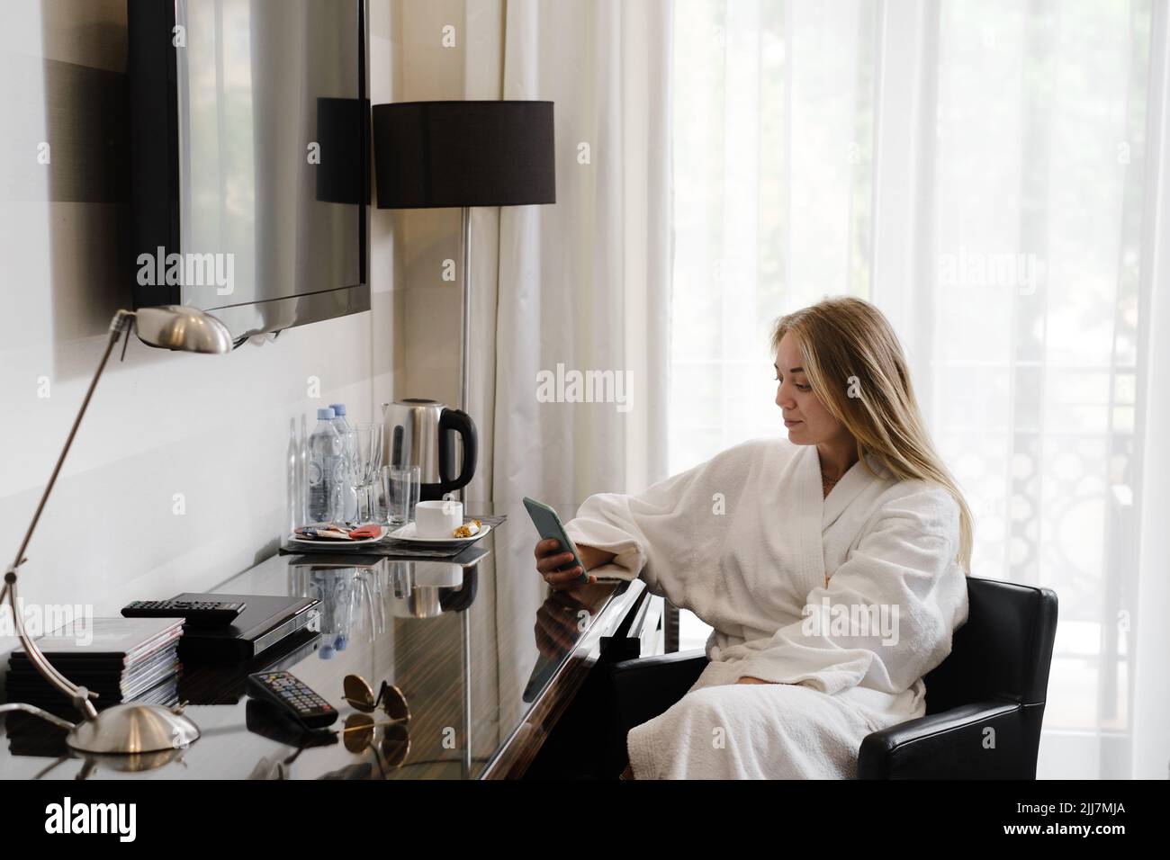Femme portant un peignoir dans la chambre d'hôtel à l'aide d'un smartphone. Communication, commande de service, achat en ligne pendant les déplacements. Personne dans Banque D'Images
