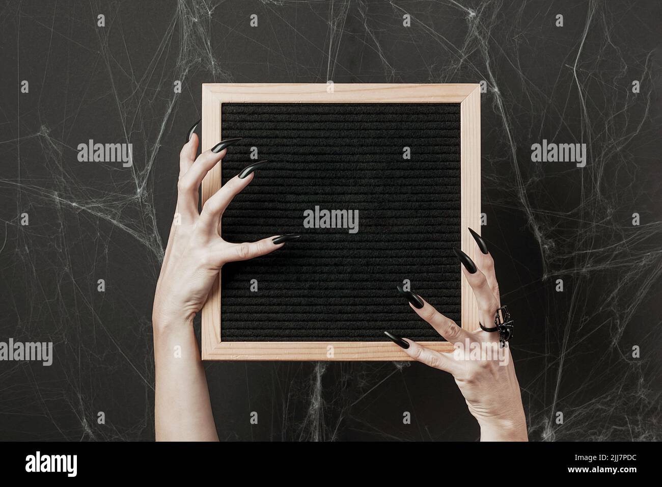 Maquette d'Halloween. Tableau de lettres dans les mains avec de longs ongles noirs et un anneau d'araignée sur fond noir avec toile de araignée. Vue avant. Banque D'Images