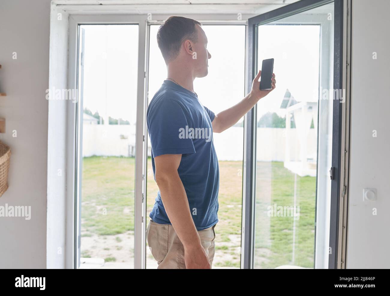 Un jeune homme prend un selfie sur le fond d'une grande fenêtre dans sa maison. Un homme tient un smartphone entre ses mains et le regarde. Photo de haute qualité Banque D'Images