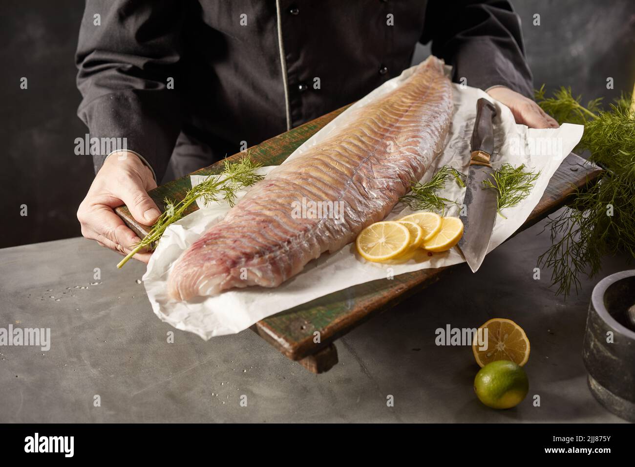 Par-dessus le chef méconnaissable avec filet de poisson frais sur planche à découper en bois dans la cuisine Banque D'Images
