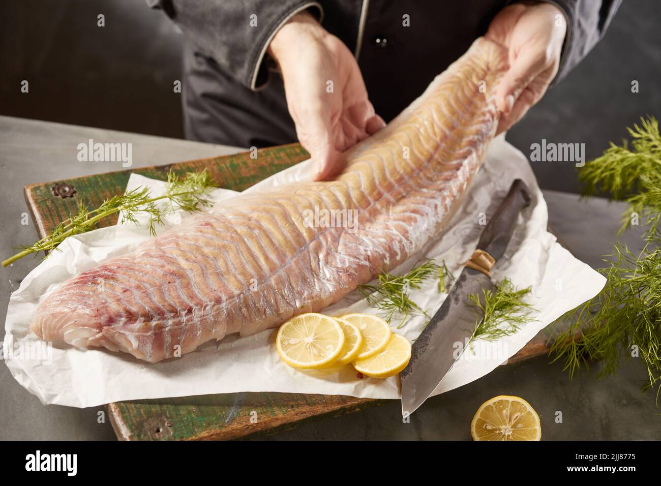 Du dessus de la récolte, un chef masculin méconnaissable avec un filet de poisson cru placé sur la planche à découper avec du citron et de l'aneth dans la cuisine Banque D'Images