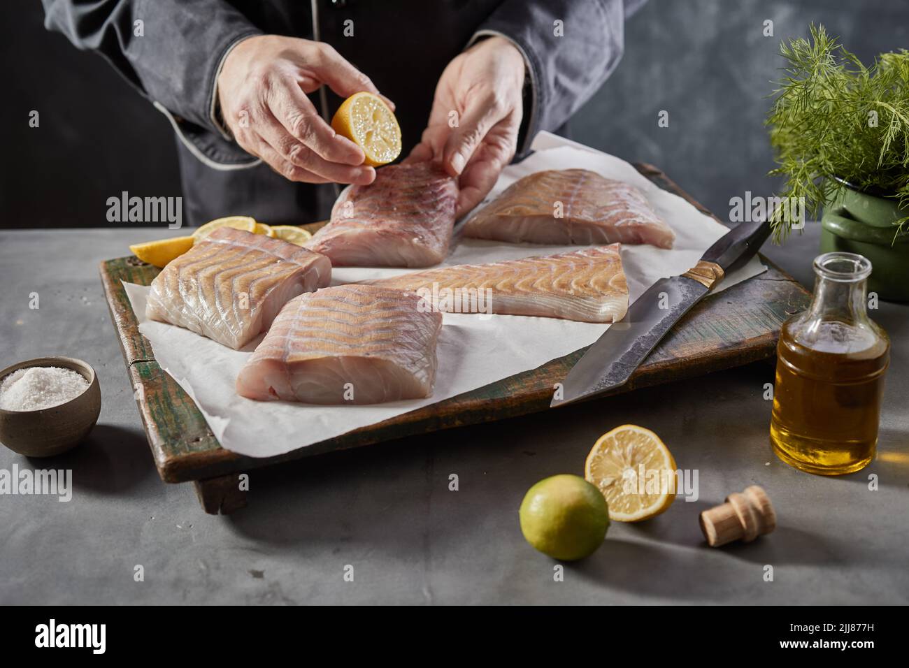 De dessus de la récolte anonyme mâle cuire en ajoutant le jus de citron sur le filet de poisson cru tout en préparant un plat savoureux dans la cuisine Banque D'Images