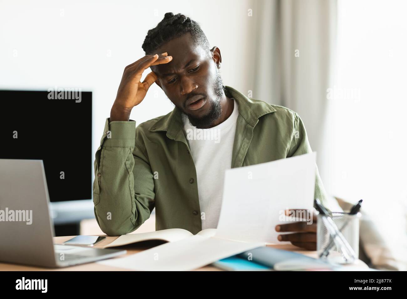 Un gars noir contrarié assis à la table du bureau à domicile, lisant le courrier et touchant son front, a obtenu de mauvaises nouvelles, l'espace de copie Banque D'Images