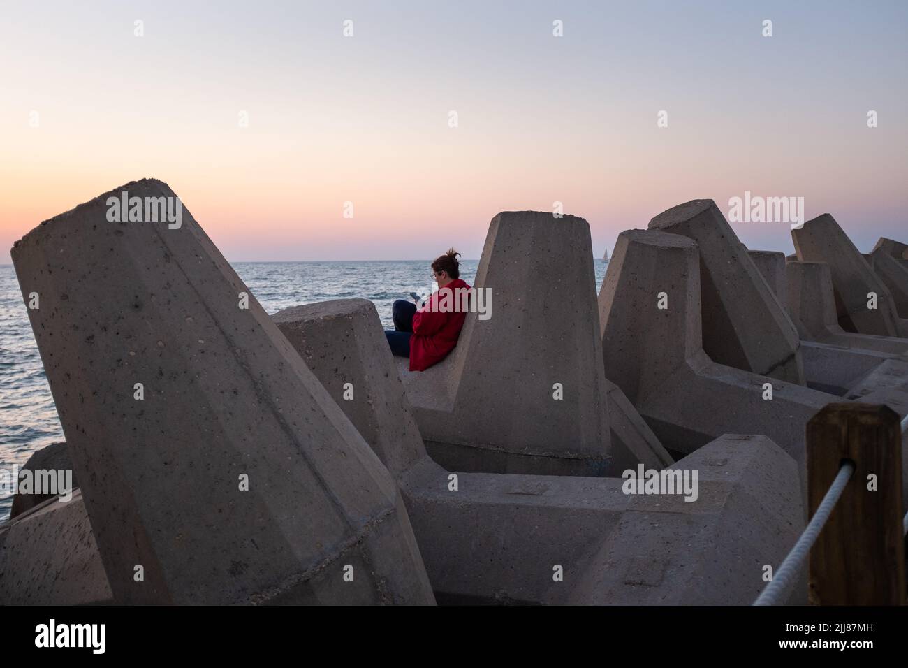 Une femme se détend sur des fortifications en béton le long d'un quai près de la mer. Banque D'Images