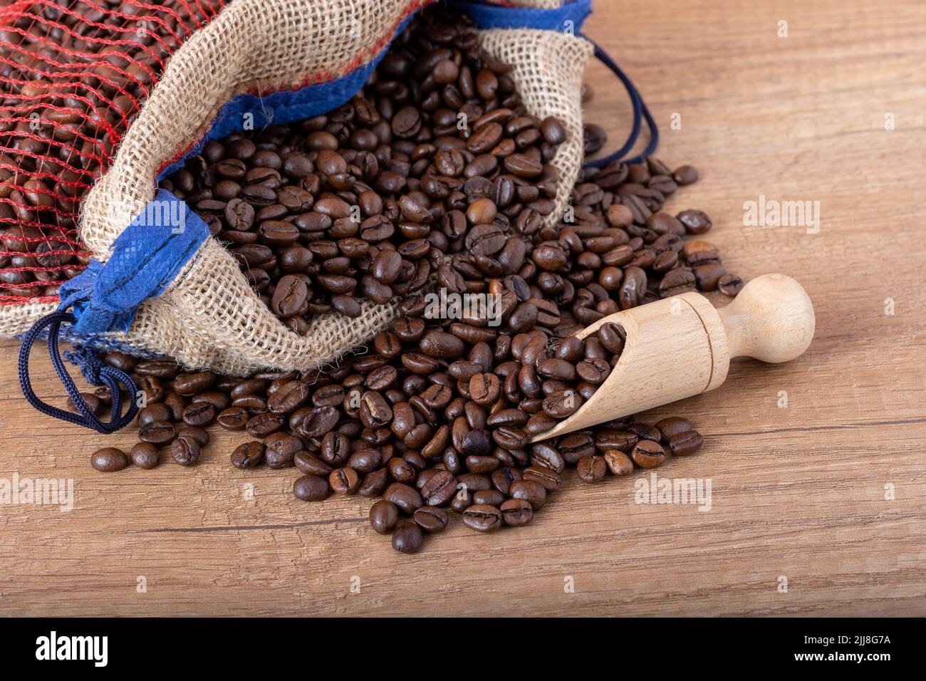 Grains de café noirs rôtis avec une cuillère en bois, qui se répande du sac sur la table. Photo pour un café, un café ou un restaurant. Banque D'Images