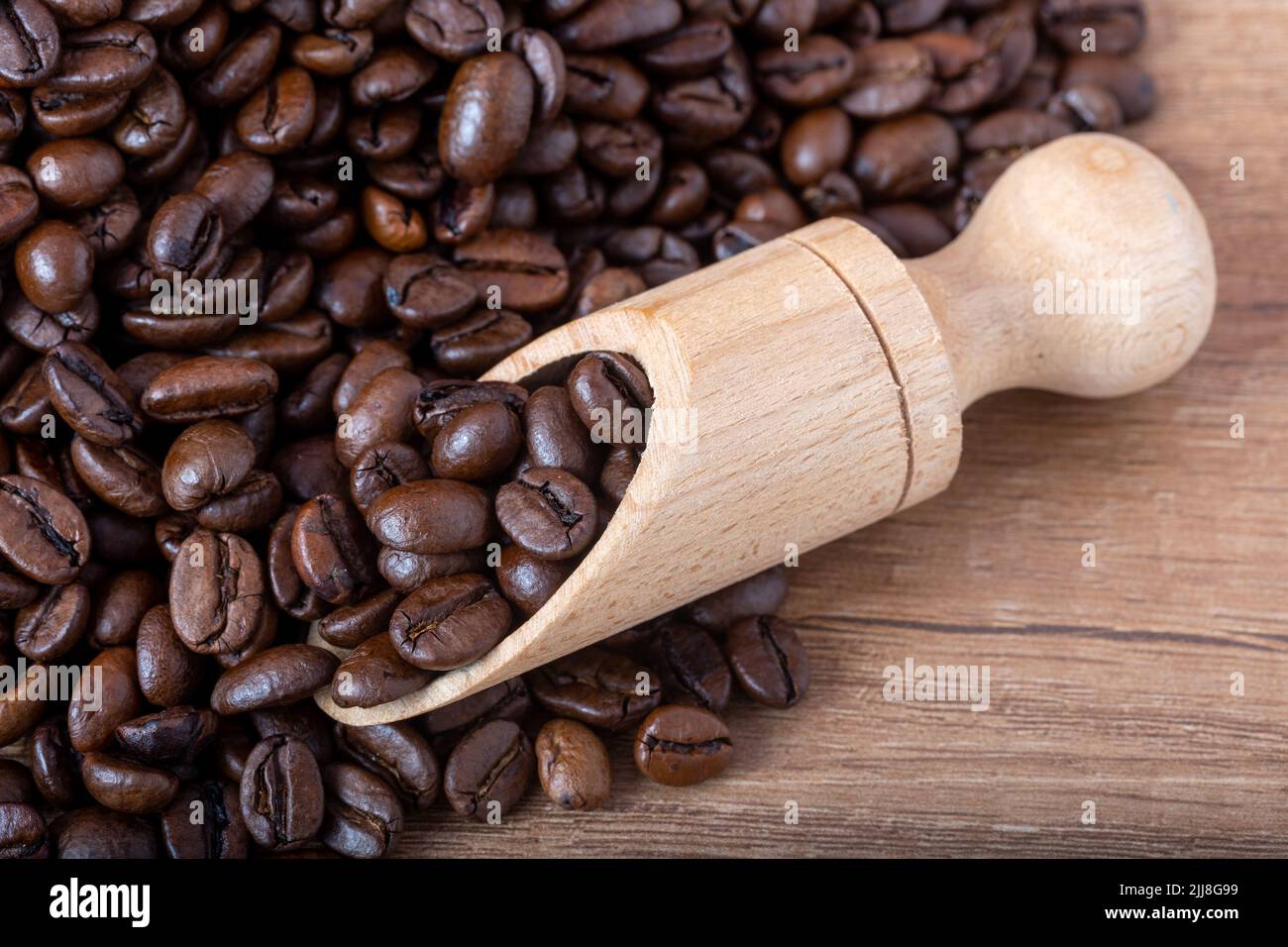 Grains de café noirs rôtis avec une cuillère en bois versant sur la table. Photo pour un café, un café ou un restaurant. Banque D'Images