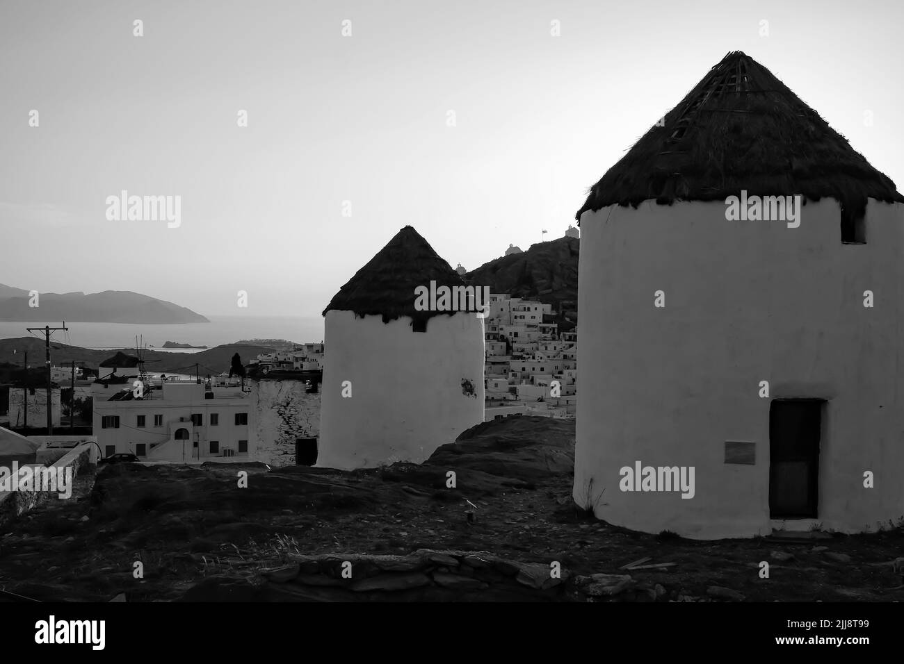 Vue sur un magnifique moulin à vent blanc illuminé, tandis que le soleil se couche de façon spectaculaire derrière le village d'iOS en Grèce, en noir et blanc Banque D'Images