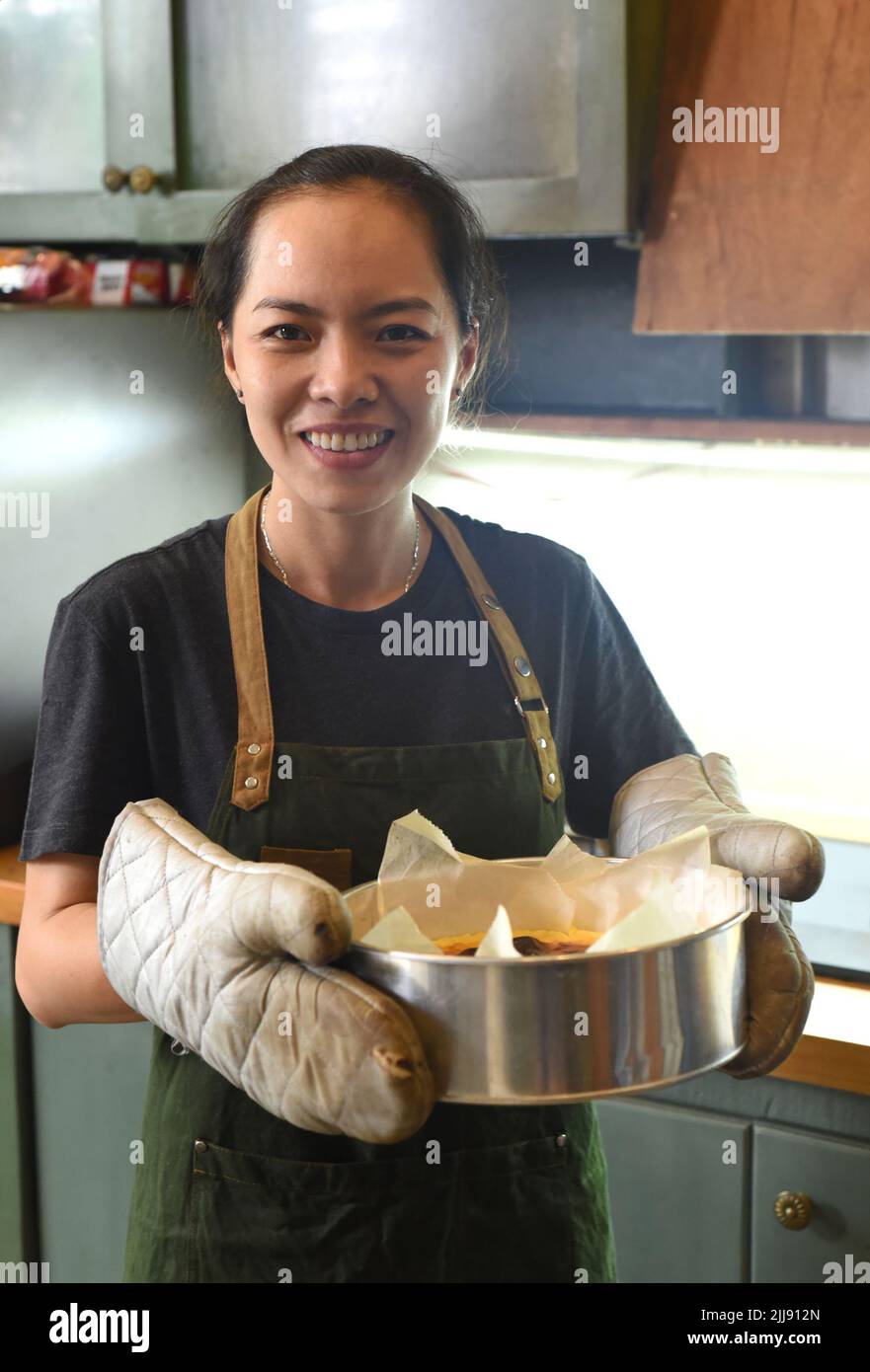 Femme vietnamienne tenant un plat de cuisson avec de la pâte au cheesecake dans la cuisine Banque D'Images