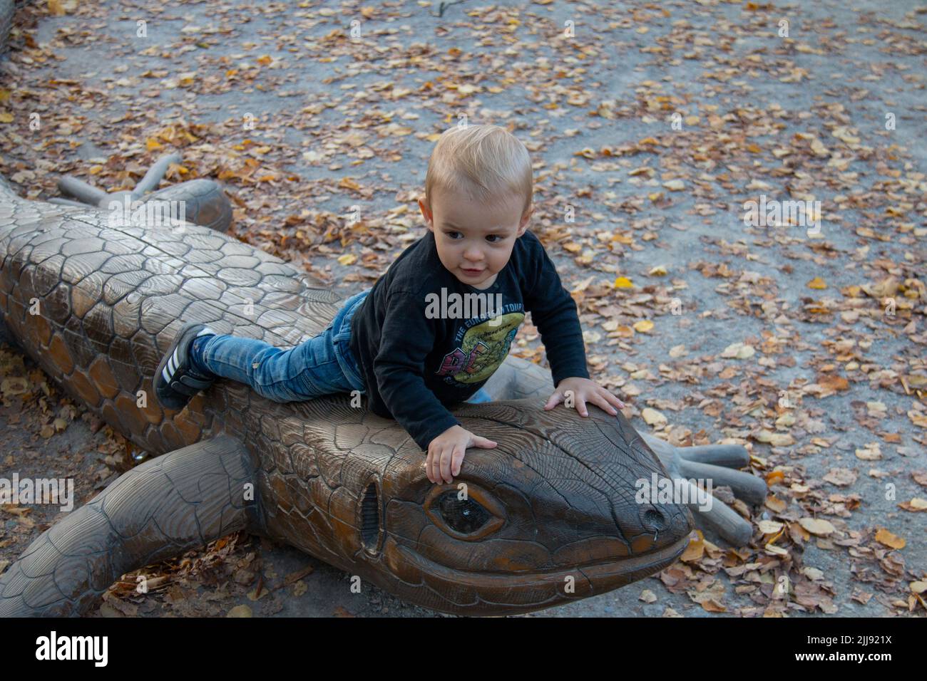 Petit garçon tout-petit à cheval animal statue de lézard en bois au terrain de jeu pour enfants Schönbrunn Zoo, Vienne, Autriche Banque D'Images