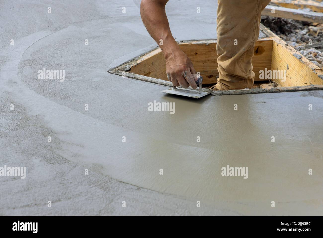 Un ouvrier de la construction utilisant un bord en acier inoxydable sur le ciment humide formant un coin au nouveau plancher de ciment Banque D'Images