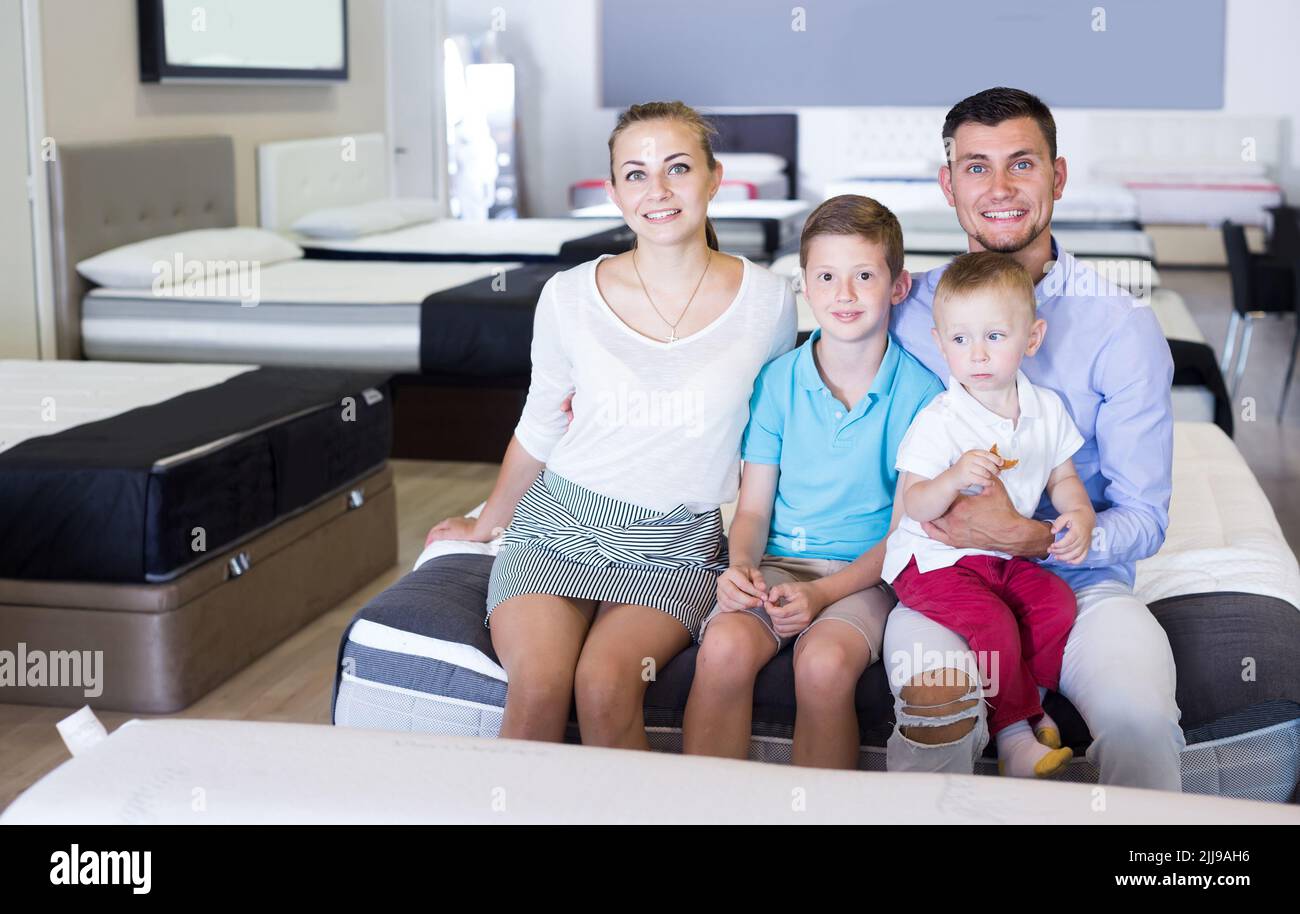 famille de quatre personnes assise sur le lit dans le salon de meubles, choix du bon matelas Banque D'Images