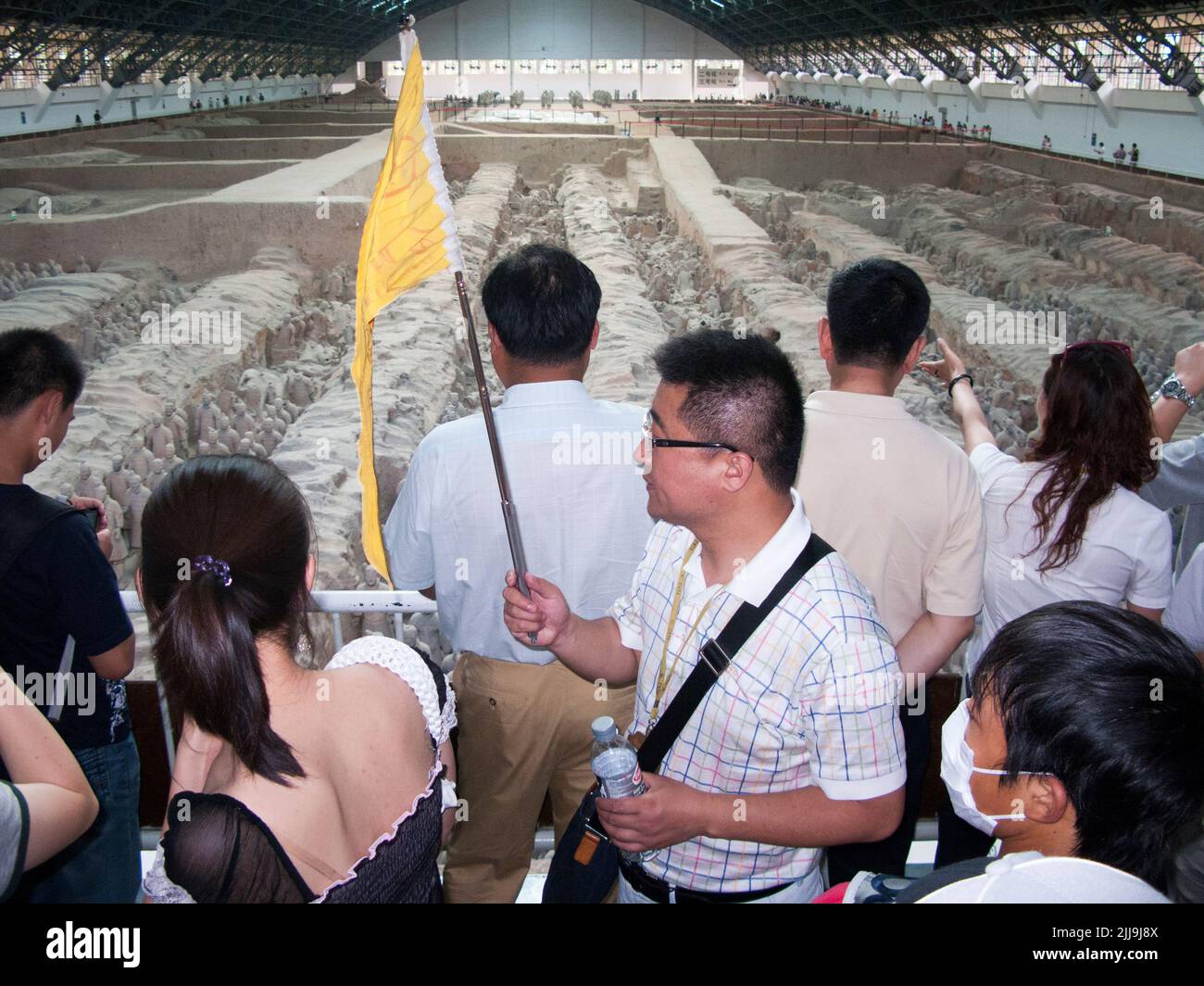 Guide touristique avec un drapeau aux couleurs vives qui mène à une fête de touristes chinois visitant / observant le stand 1 de l'armée de terre cuite au musée du Mausolée de l'empereur Qinshihuang à Xi'an, en Chine. PRC. (125) Banque D'Images