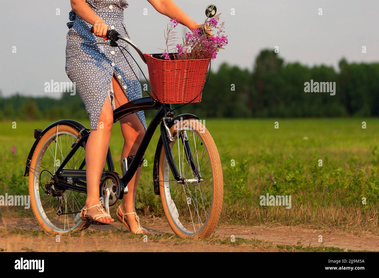 Femme en robe bleue à cheval sur un vélo noir dans un terrain d'été Banque D'Images