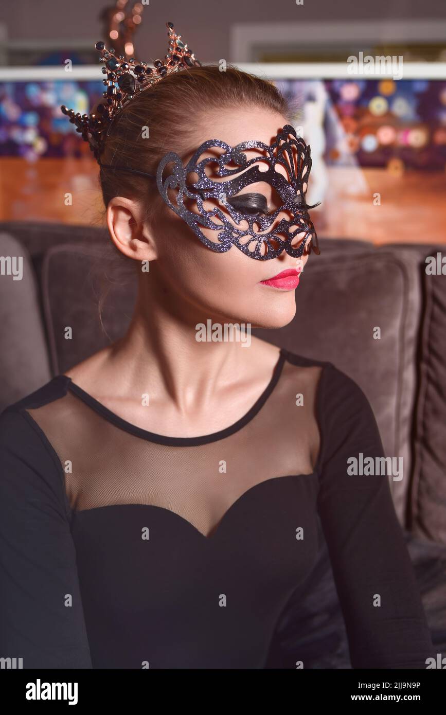 Portrait d'un beau modèle portant une couronne et un masque de carnaval dans une robe noire dans le studio Banque D'Images