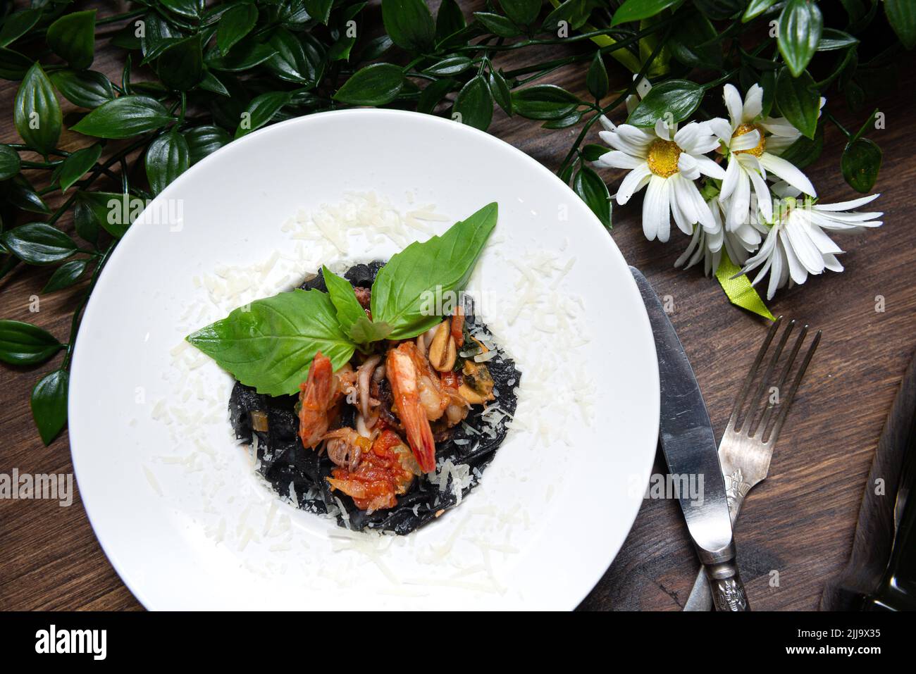 Assiette de pâtes à l'encre de seiches et aux fruits de mer, au parmesan râpé, garnie de feuilles de basilic frais. Vue de dessus. Banque D'Images