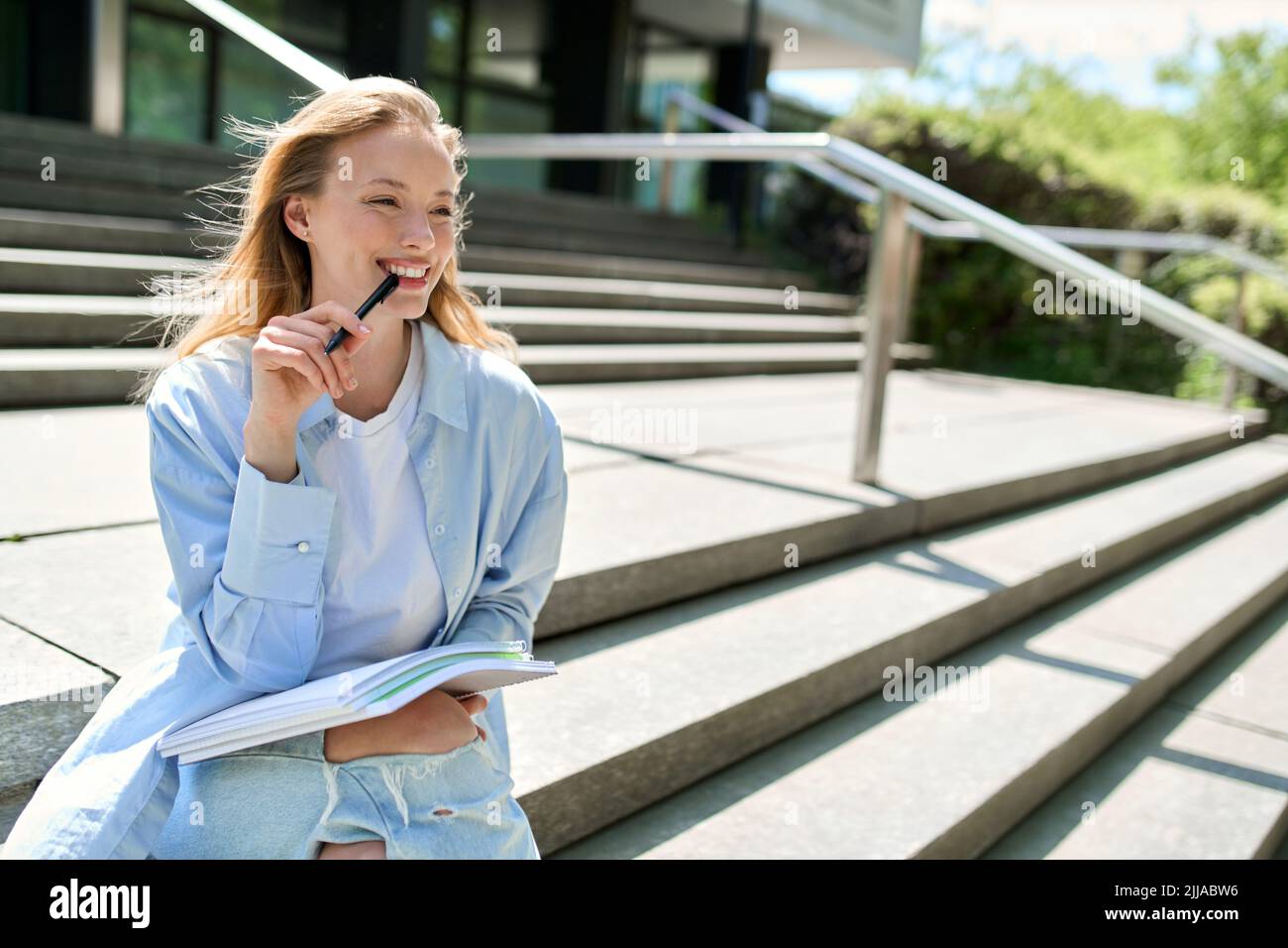 Jeune fille souriante étudiant de l'université tenant des carnets assis sur les escaliers à l'extérieur. Banque D'Images
