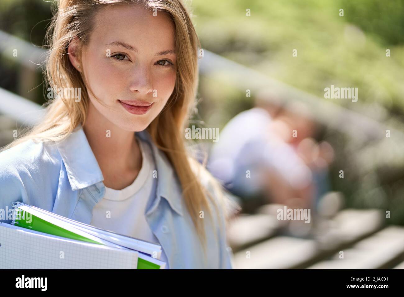 Souriante jolie fille étudiante à l'université regardant l'appareil photo, portrait à l'extérieur. Banque D'Images