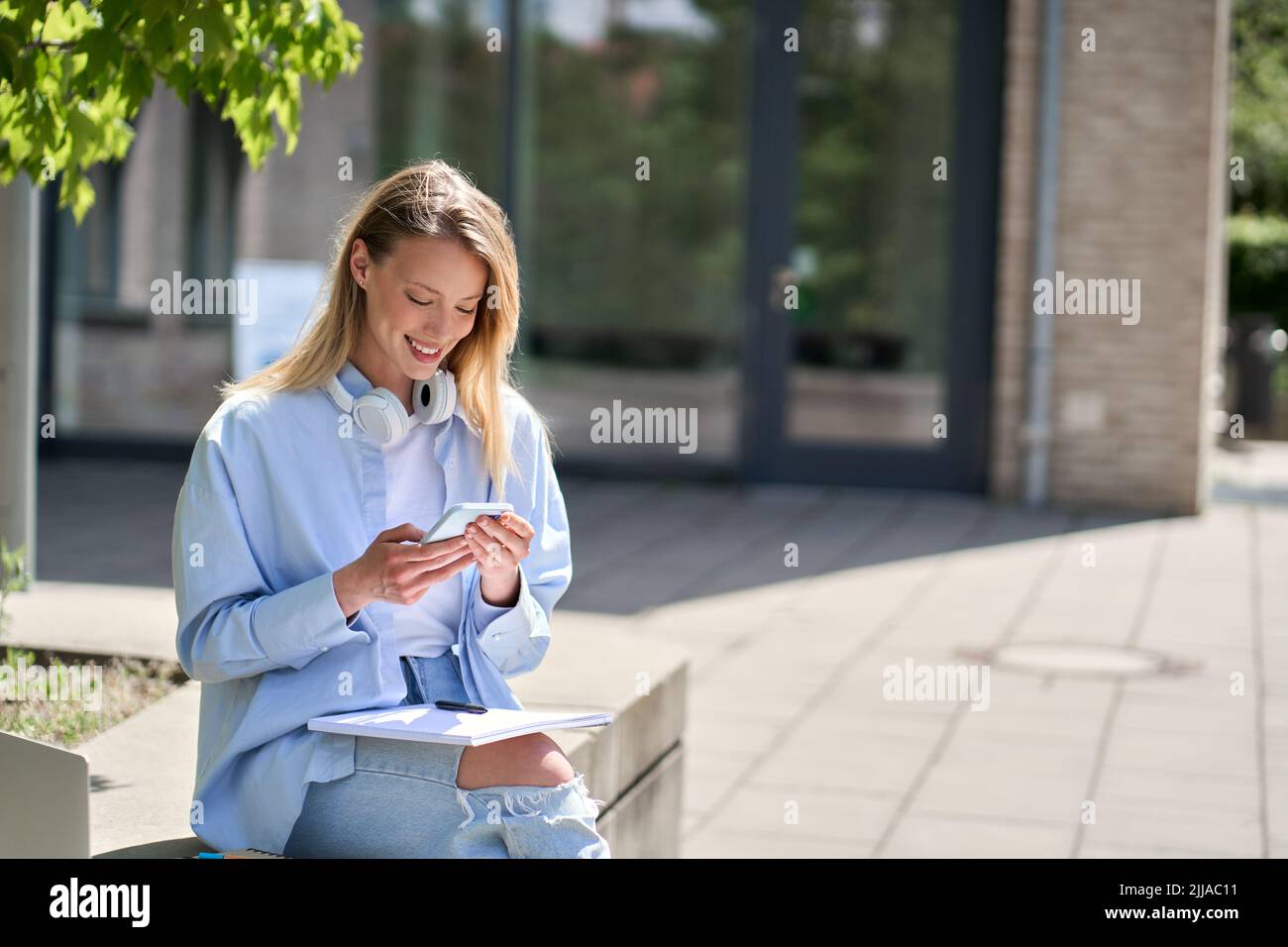 Belle fille heureuse étudiante à l'université en utilisant le téléphone mobile assis à l'extérieur. Banque D'Images