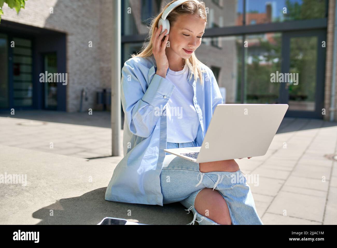 Une jeune étudiante de l'université portant un casque à l'aide d'un ordinateur portable apprentissage en ligne à l'extérieur. Banque D'Images