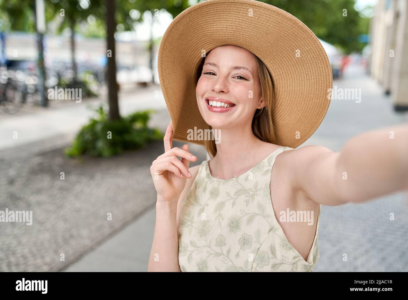 Jeune femme heureuse portant un chapeau emportant un selfie dans la rue estivale de la ville. Banque D'Images