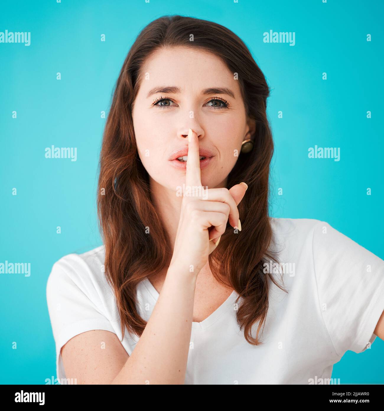 Garons cela entre nous. Portrait studio d'une jeune femme attrayante posant avec son doigt sur ses lèvres sur un fond bleu. Banque D'Images