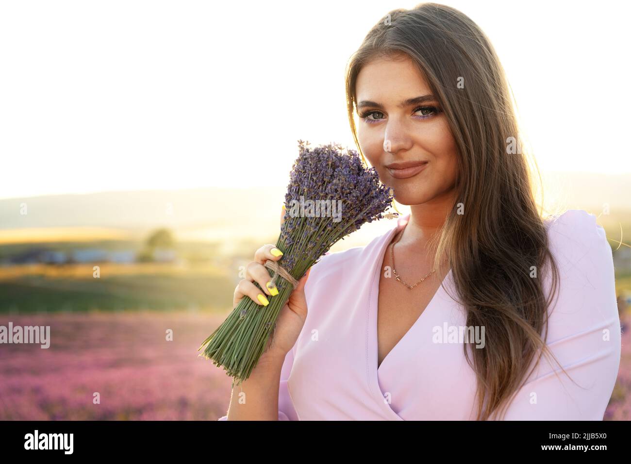 Jeune femme en robe tenant un bouquet de fleurs debout dans le champ de lavande Banque D'Images