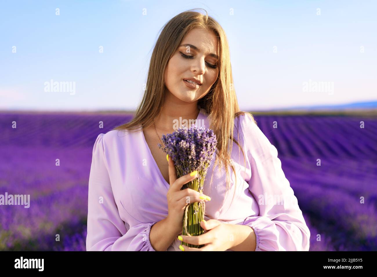 Jeune femme en robe tenant un bouquet de fleurs debout dans le champ de lavande Banque D'Images