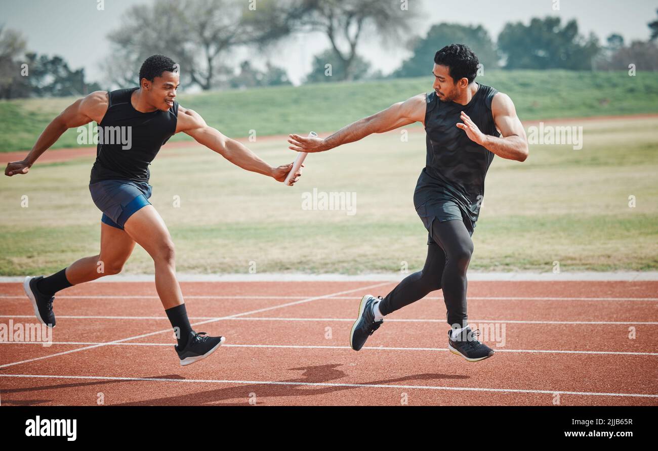 La passe parfaite. Tir en longueur d'un jeune athlète masculin saisissant un bâton de son coéquipier pendant une course de relais. Banque D'Images