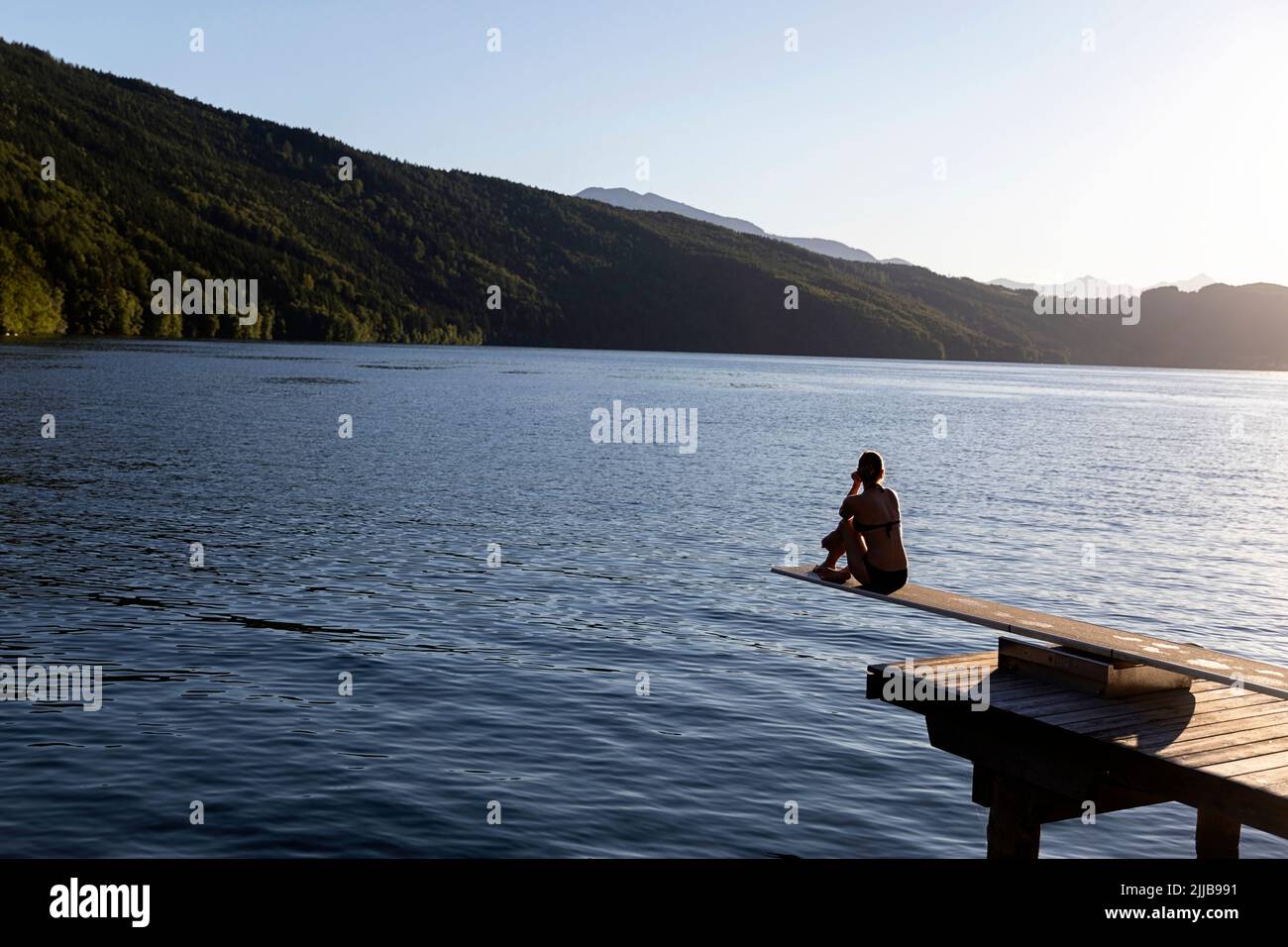 Une femme assise sur une plate-forme de plongée sur une belle jetée en bois sur le lac Millstätter See au coucher du soleil, Carinthie, Autriche Banque D'Images