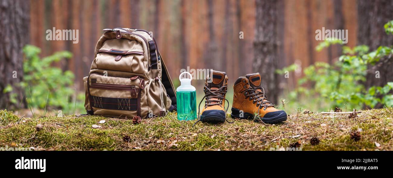 Matériel de randonnée et de camping en forêt. Sac à dos, bouteille d'eau et bottines en cuir. Vue panoramique avec espace de copie Banque D'Images