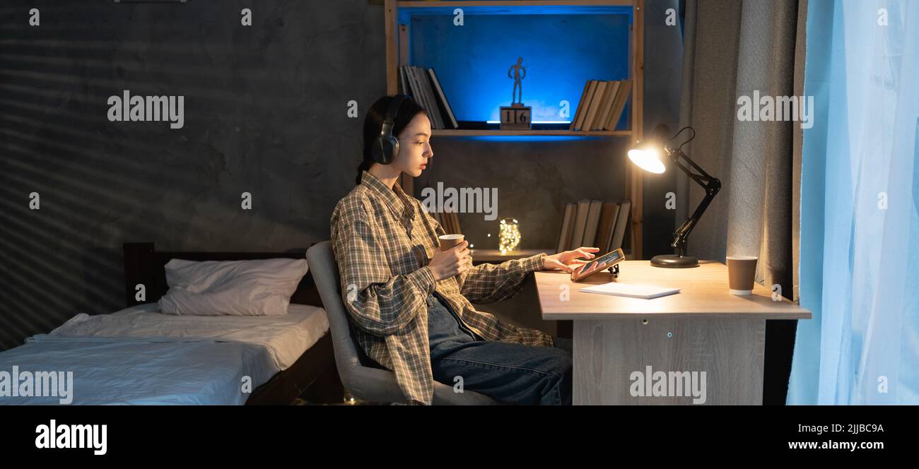 une jeune fille asiatique utilise le tablet pc et les écouteurs numériques le soir, regarde un film ou écoute de la musique à la maison le soir Banque D'Images