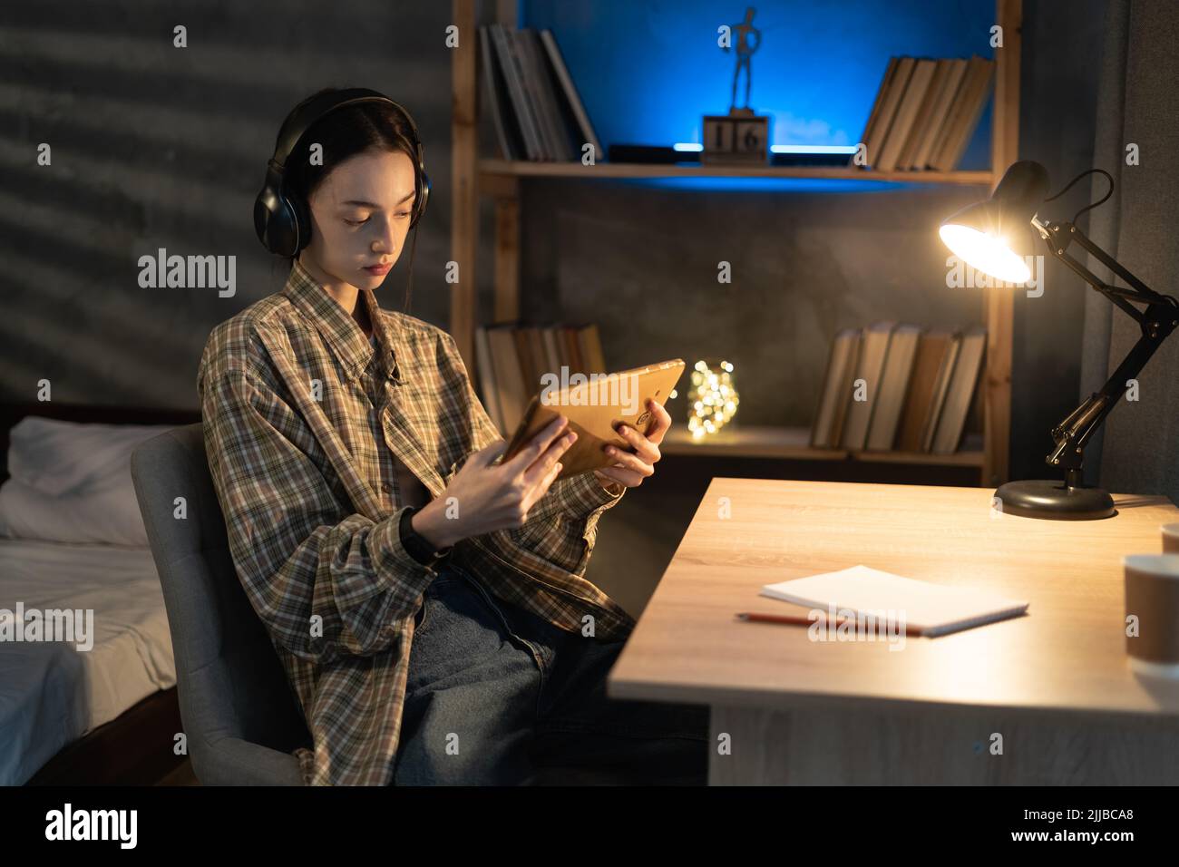 une jeune fille asiatique utilise la tablette numérique et les écouteurs le soir, regarde un film ou écoute de la musique à la maison Banque D'Images