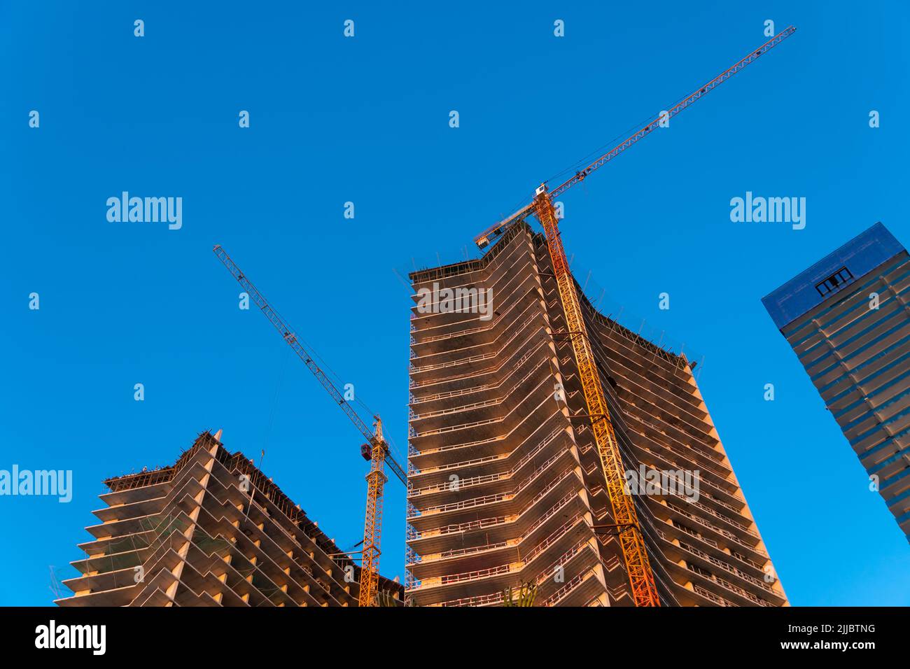 Bâtiments de plusieurs étages en construction avec grues de construction contre le ciel bleu au coucher du soleil Banque D'Images
