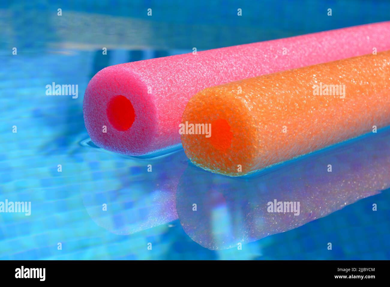 Des vibes d'été, des nouilles de bain en polyéthylène rouge et orange colorées flottent dans une piscine carrelée de bleu Banque D'Images