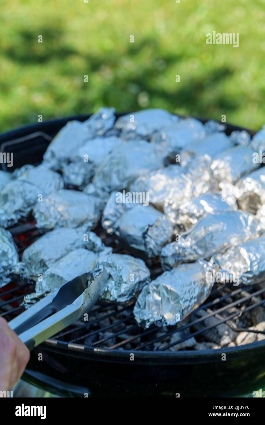 Cuisson à la maison - Déballage du maïs cuit ou cuit sur le gril de bois de chauffage enveloppé dans du papier aluminium Banque D'Images