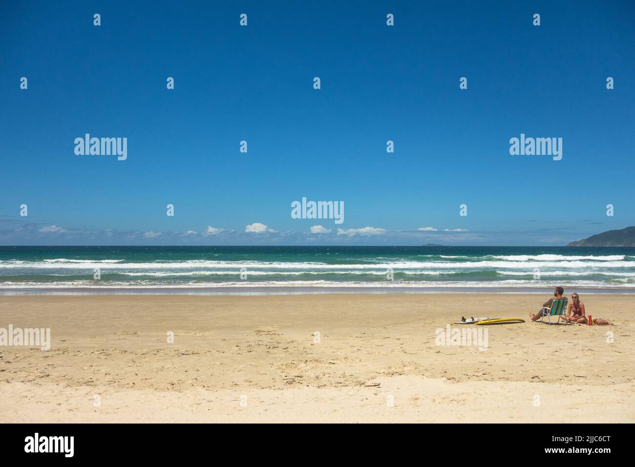 Un couple de surfeurs appréciant un bain de soleil assis sur le sable près de deux planches de surf. Calme mer bleu ciel propre plage agréable endroit frais chill Vibe romance, Banque D'Images