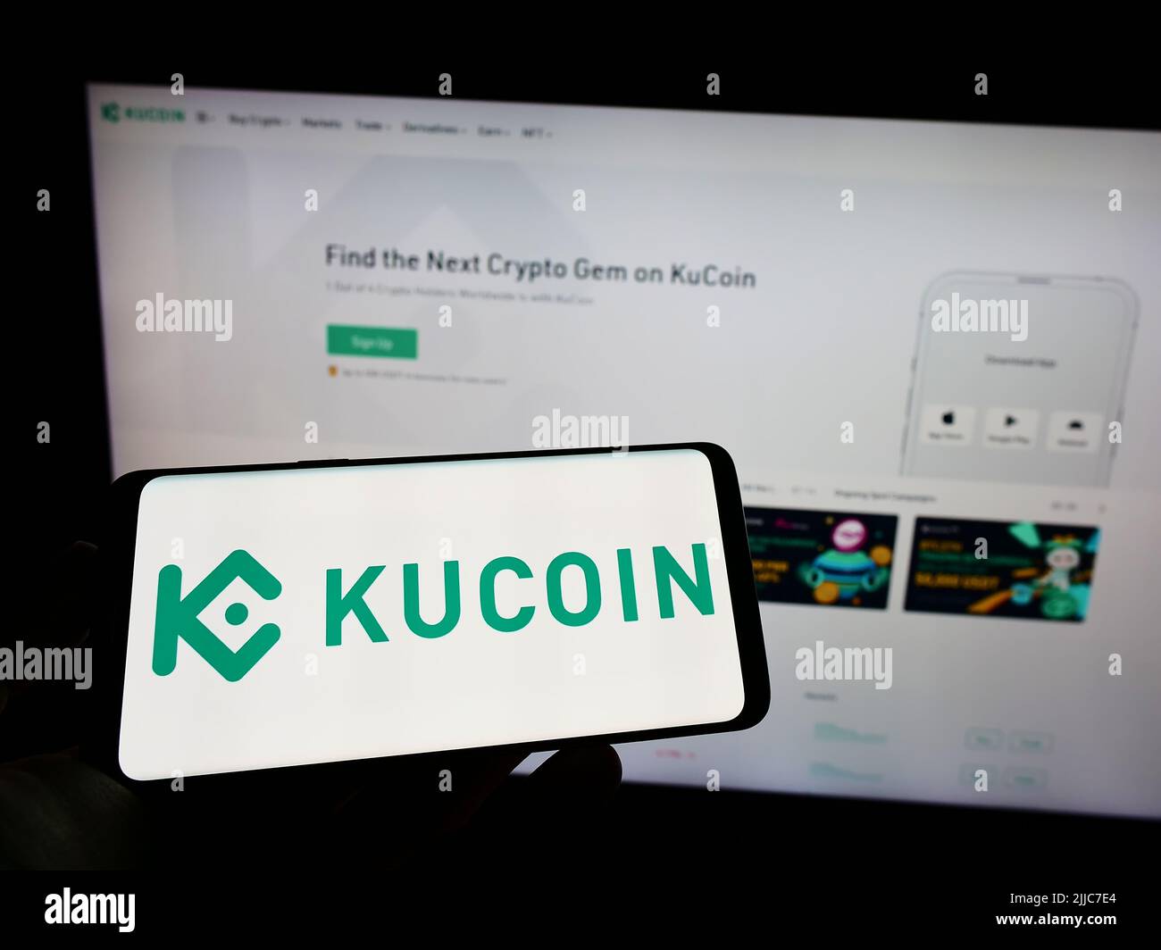 Personne tenant un téléphone portable avec le logo de la société d'échange cryptographique Kucoin sur l'écran en face de la page Web d'affaires. Mise au point sur l'affichage du téléphone. Banque D'Images