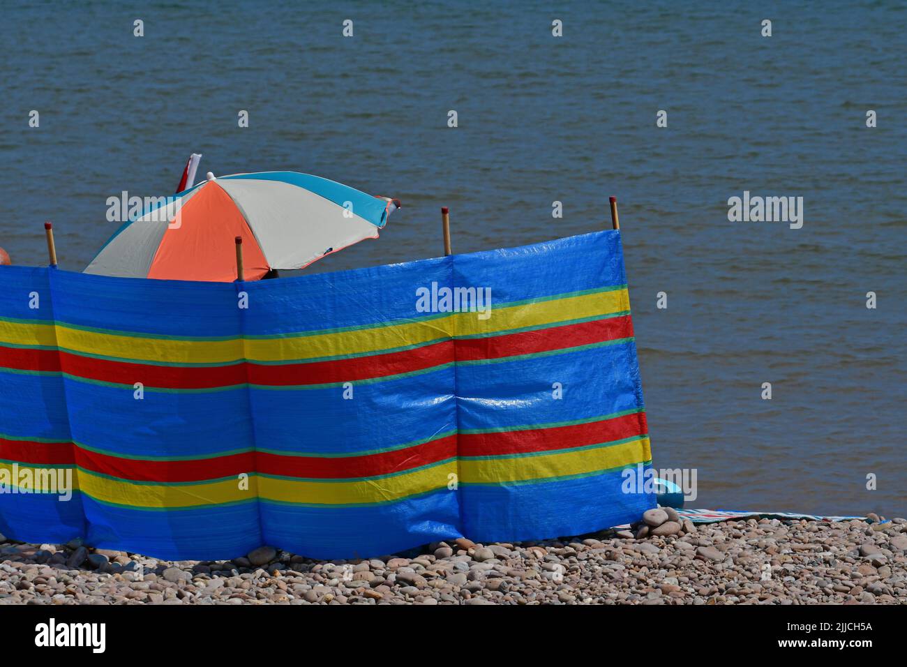 Coupe-vent rouge bleu et jaune avec unbrella sur la plage à Sidmouth dans East Devon. Image de stock .Robert Timoney. Banque D'Images