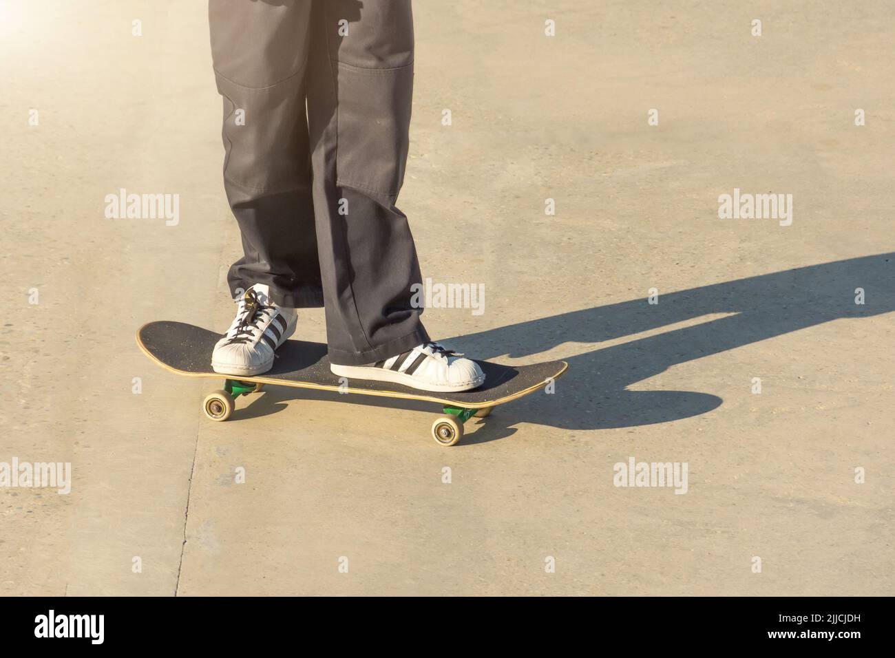 Guy en Jean cargo noir et baskets se déplace sur un sol en béton avec un skateboard, mettant son pied dessus Banque D'Images