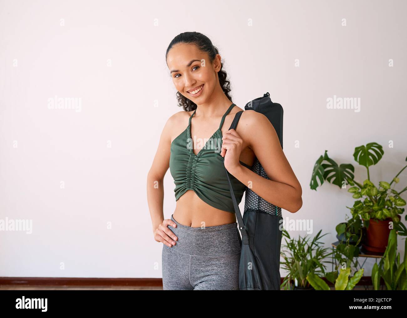 Une jeune femme multi-ethnique se tient avec son sac de tapis de yoga dans un studio rempli de plantes Banque D'Images